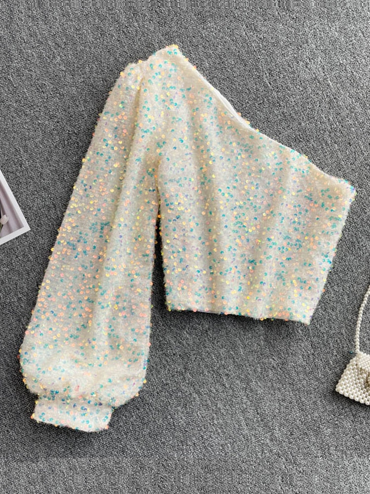 Saffron glitter one-shoulder top: voeg glamour toe aan je avondlook met sprankelende pailletten en een trendy asymmetrisch ontwerp. Perfect voor feestjes en speciale gelegenheden. Verkrijgbaar in goud, wit en blauw/goud. Combineer met rokken, broeken of jeans voor veelzijdige styling. Comfortabele pasvorm en opvallend design voor een zelfverzekerde uitstraling. Bestel nu en laat je stijl stralen!